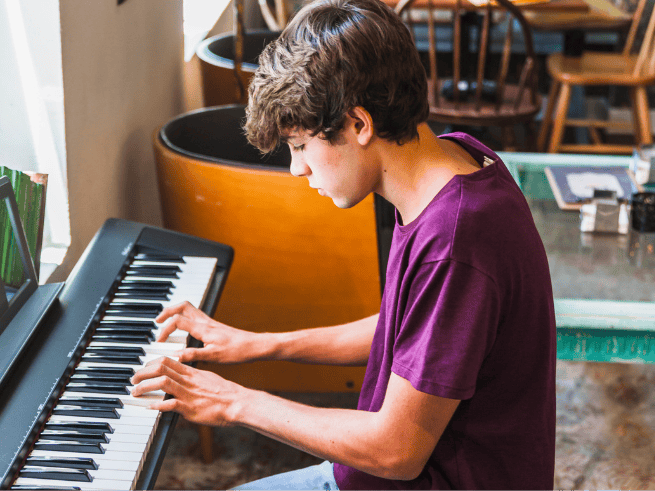 Teenager playing an electric keyboard during an online music class, perfect for learning online keyboard lessons.